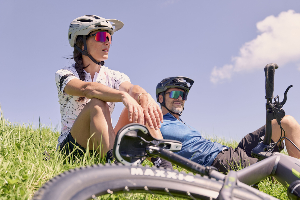 A woman and a man sit in a meadow with their rental bikes next to them