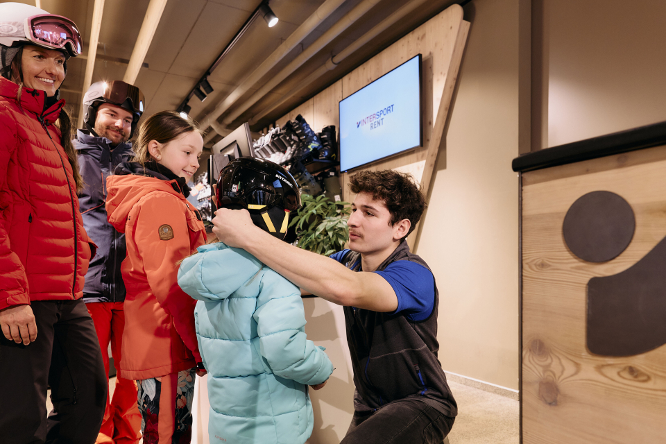Mitarbeiter hilft einem Kind beim Anziehen des Skihelms