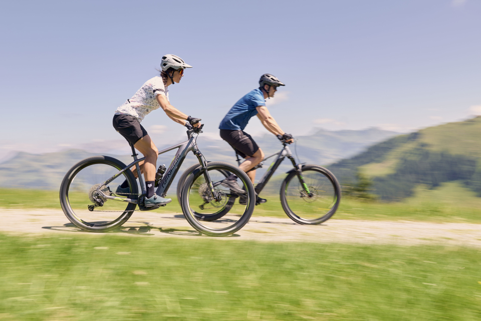 Two cyclists ride their e-bikes down a gravel road