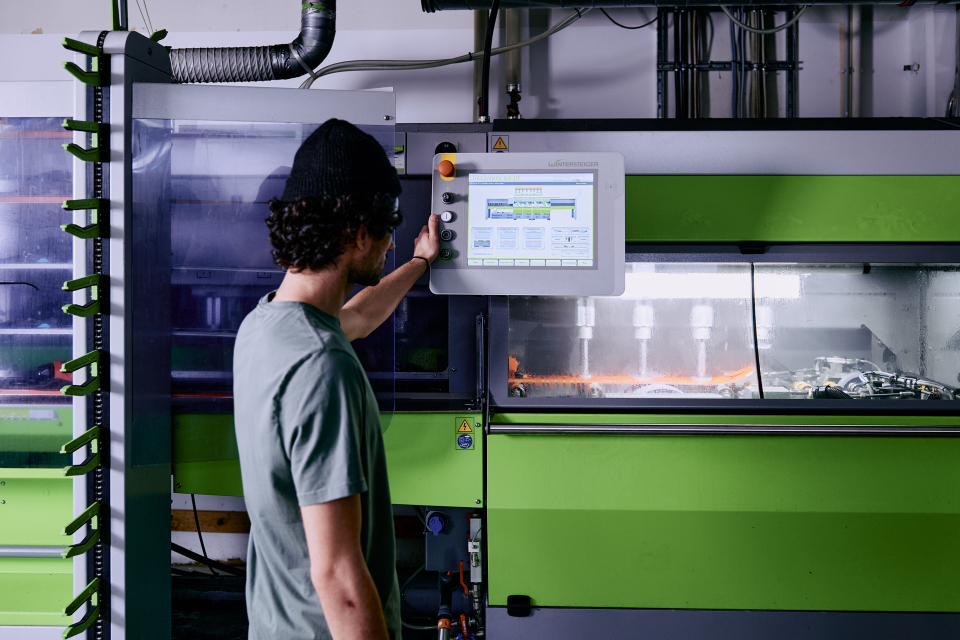 Mitarbeiter steht vor einer grünen Skiservicemaschine