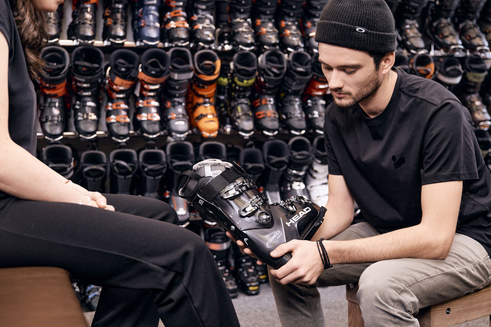 Employee holding a ski boot in his hand, with a wall of ski boots visible in the background