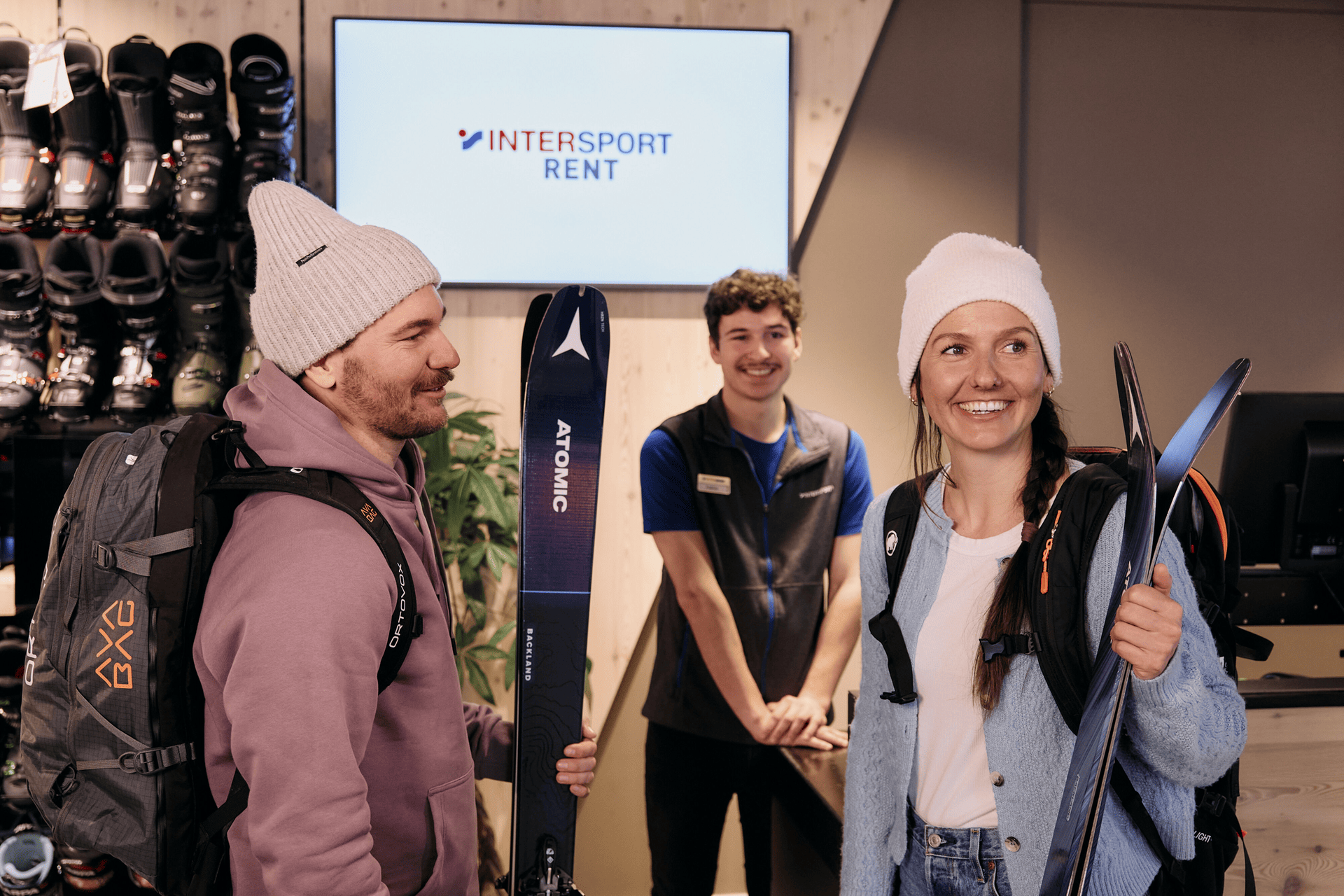 Two customers are standing in the shop holding skis in their hands, with an employee standing in the background