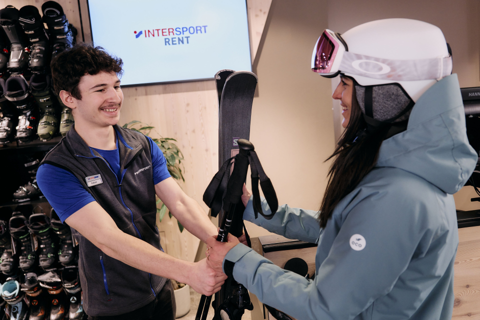An employee hands a woman her rental skis and poles